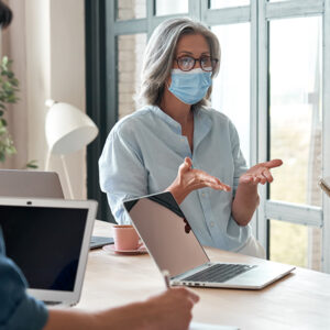 Woman wearing a mask presenting to a group.